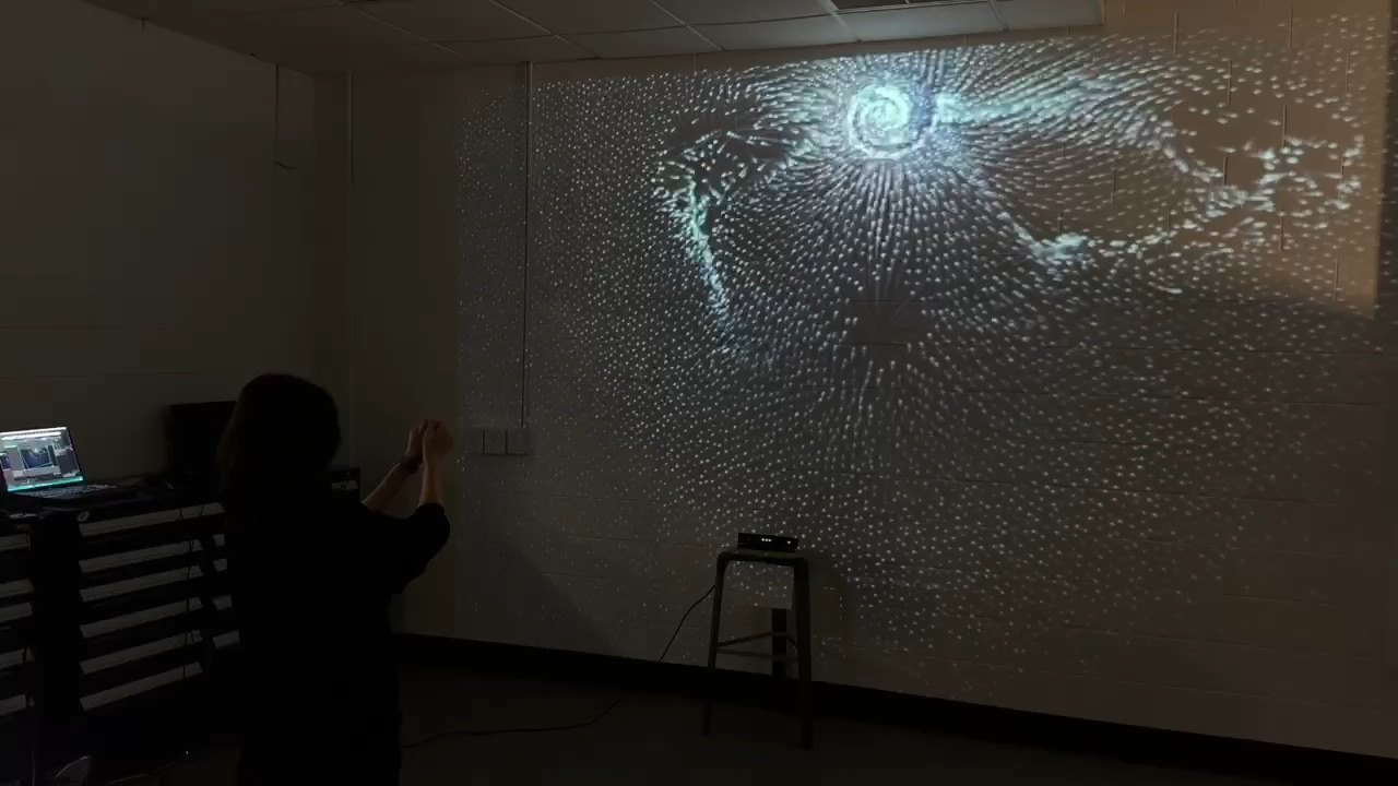 Polaris installation: a person moving their hands in front of a wall projection of swirling particles
